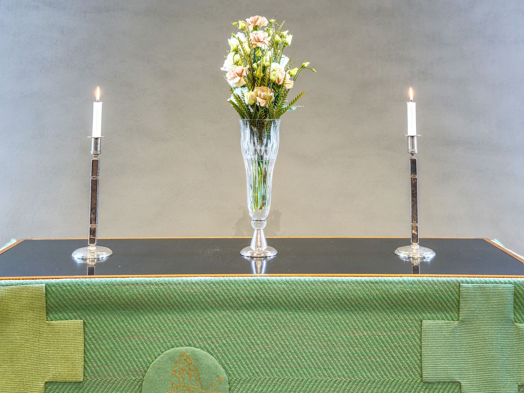 Kuvassa on Töölön kirkon alttaripöytä vihreässä liturgisessa vaatteessa. Alttarilla on kukkakimppu, jonka molemmin puolin palaa kynttilä.