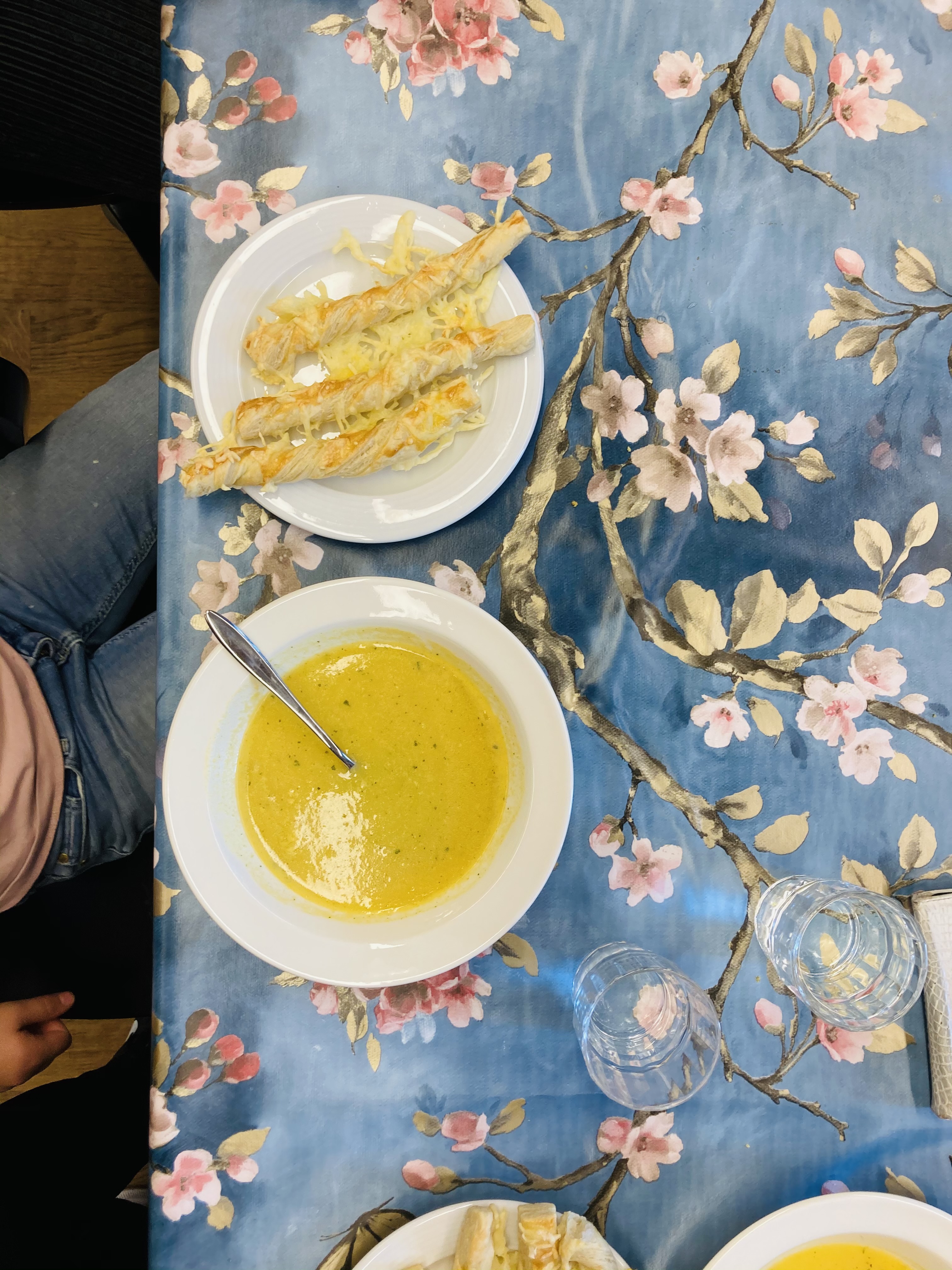 Valkoisella lautasella keltaista sosekeittoa ja vieressä lautasella kolme juustokierrettä