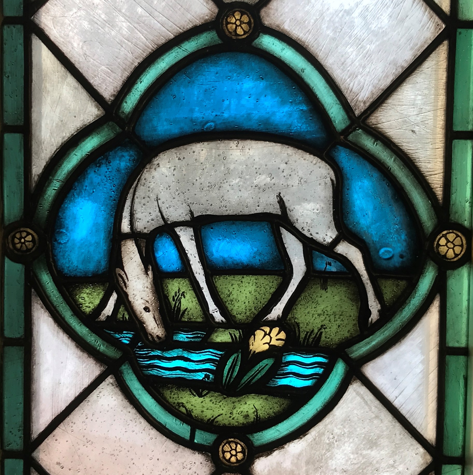 Kuvassa Töölön kirkon porraskäytävän lasimaalaus, jossa peura kumartuu juomaan purosta vettä.