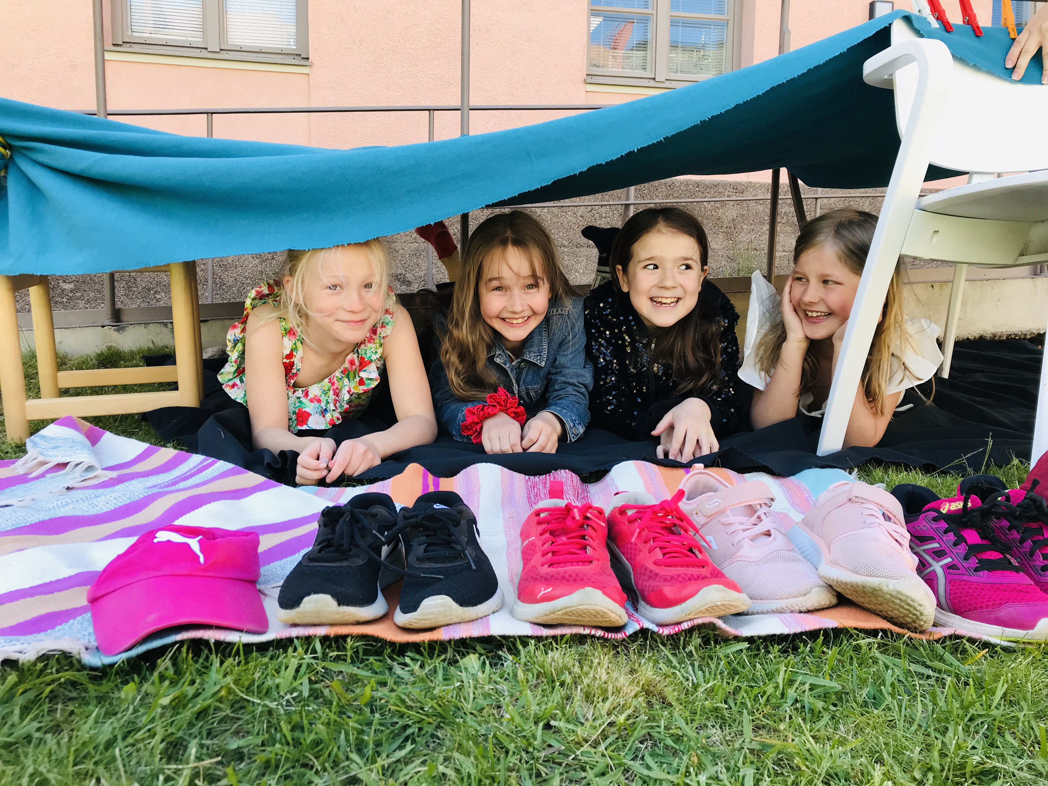 neljä tyttyö makaa itserakentamassaan majassa värikkäät kengät edessään.